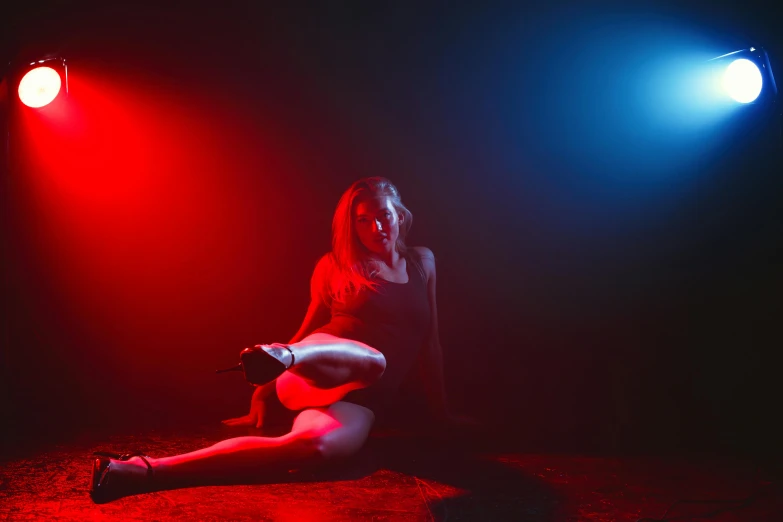 a woman sitting on the ground under a red light, red blue theme, bisexual lighting, show light, sinister pose