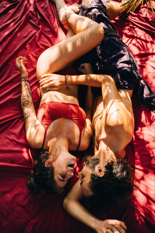 a couple of people laying on top of a bed, trending on pexels, red body suit, holding each other, warm sunshine, center of image