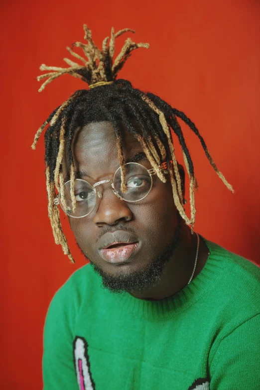 a man with dreadlocks sitting in front of a red wall, an album cover, trending on pexels, dada, green mane, with glasses on, headshot profile picture, grayish