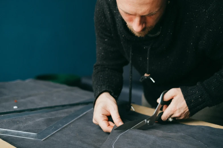 a man cutting fabric with a pair of scissors, by Matthias Stom, trending on unsplash, arbeitsrat für kunst, leather straps, repeating pattern, blue print, wearing a leather trench coat