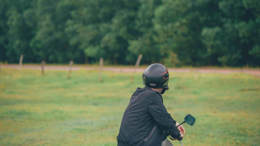 a man riding a motorcycle on a lush green field, a picture, unsplash, happening, wearing skate helmet, man sitting facing away, grey, low quality photo