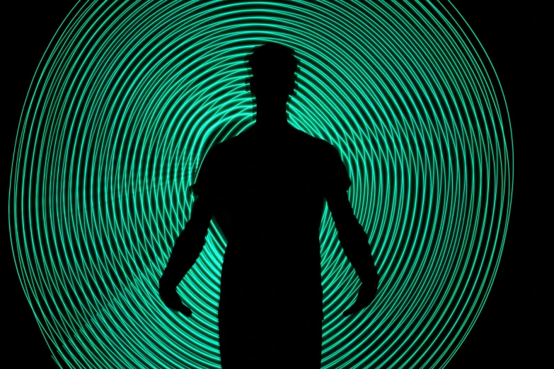 a man standing in front of a green light, by Jon Coffelt, pexels, kinetic art, glowing spiral background, outlined silhouettes, black and teal paper, doppler effect