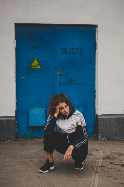 a woman squatting in front of a blue door, an album cover, inspired by Elsa Bleda, pexels contest winner, graffiti, curly haired, russia, sad man, teenage boy