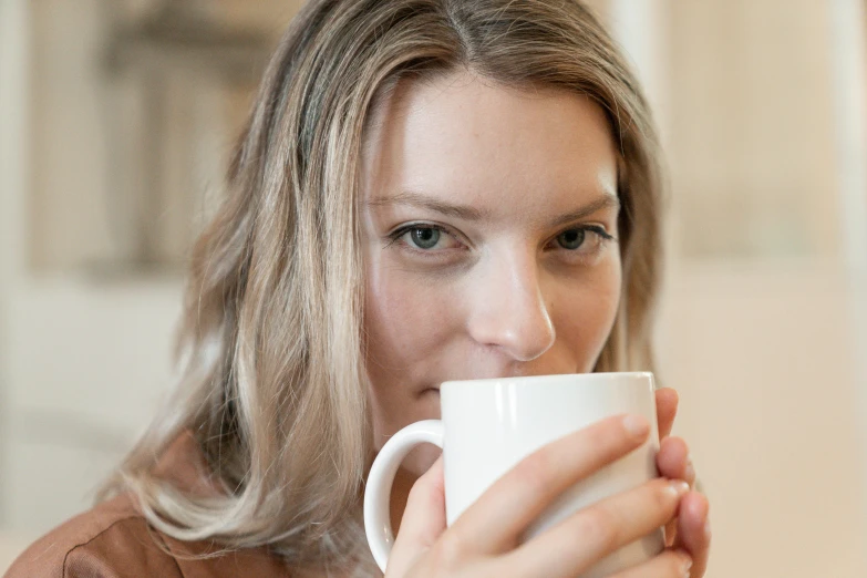 a close up of a person holding a coffee cup, by Alice Mason, attractive face, blonde, white, tea