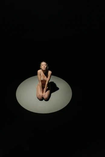 a woman sitting on a circle in the dark, inspired by Vanessa Beecroft, video art, sunbathed skin, mini model, high angle, high quality photo