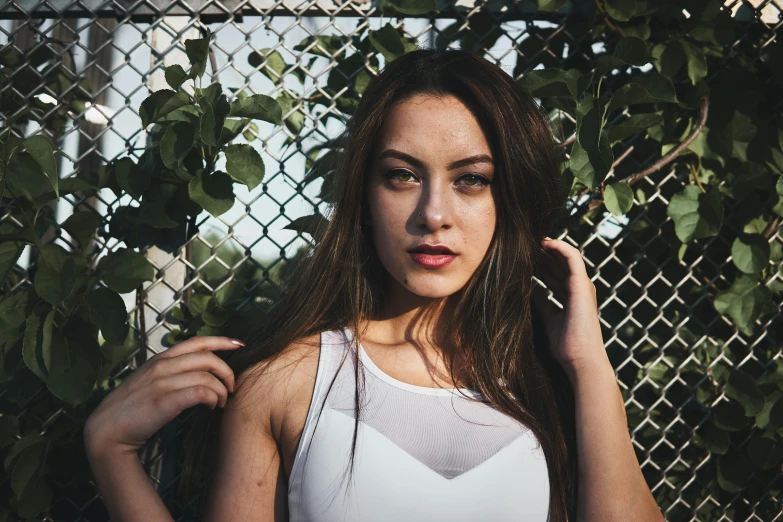 a beautiful young woman standing in front of a fence, inspired by Elsa Bleda, pexels contest winner, renaissance, wearing a tanktop, portrait sophie mudd, loosely cropped, an all white human