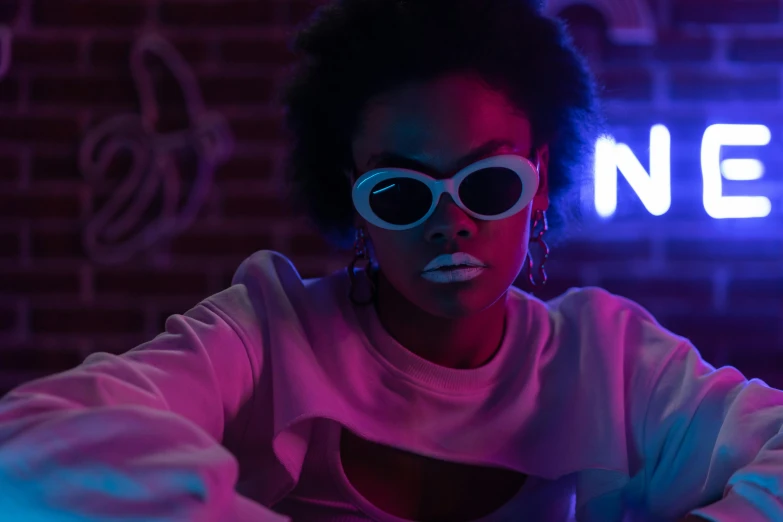 a woman sitting in front of a neon sign, trending on pexels, afrofuturism, neo noir, digital sunglasses, reflecting light in a nightclub, nerdy black girl super hero