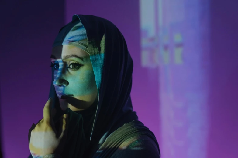 a woman with blue paint on her face talking on a cell phone, a hologram, by Maryam Hashemi, face is wrapped in a black scarf, purple and cyan lighting, cinematic light and reflections, ameera al taweel