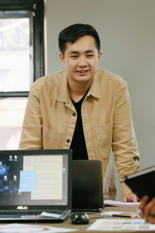 a group of people sitting around a table with laptops, a picture, by Reuben Tam, standing on a desk, asian male, slightly smiling, photo of a man