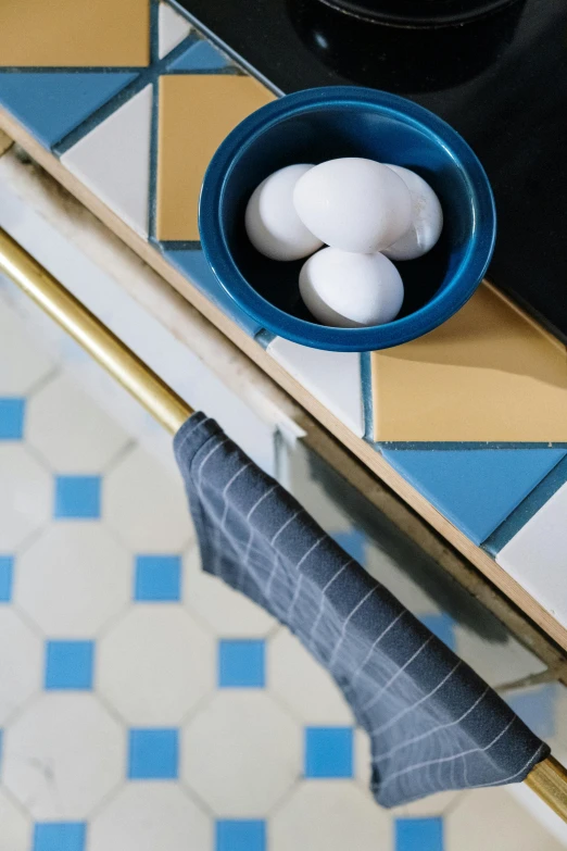 a blue bowl filled with eggs sitting on top of a counter, towels, tiles, detail shot, ignant