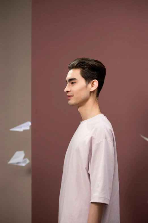 a man standing in front of a bunch of paper airplanes, an album cover, inspired by Russell Dongjun Lu, trending on pexels, portrait of beautiful young man, ( side ) profile, nonbinary model, wearing a linen shirt