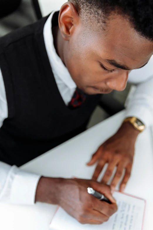 a man sitting at a desk writing on a piece of paper, pexels contest winner, dark skinned, praying, elegantly dressed, thumbnail