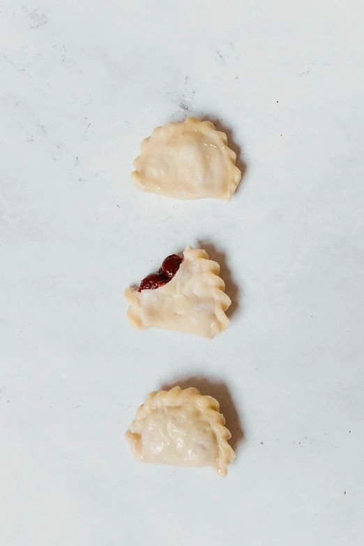 a close up of three pastries on a table, inspired by Károly Patkó, on a gray background, mouth half open, garnet, top-down view