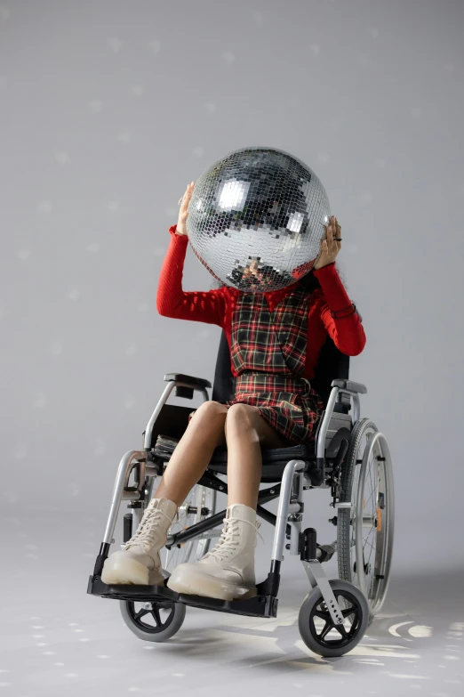 a person in a wheelchair with a disco ball on their head, an album cover, inspired by Yayou Kusama, shutterstock contest winner, patricia piccinini, speculative fashion, holiday season, star child