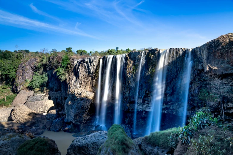 a large waterfall in the middle of a forest, by Peter Churcher, pexels contest winner, hurufiyya, blue sky, ethiopian, avatar image, kailasa temple