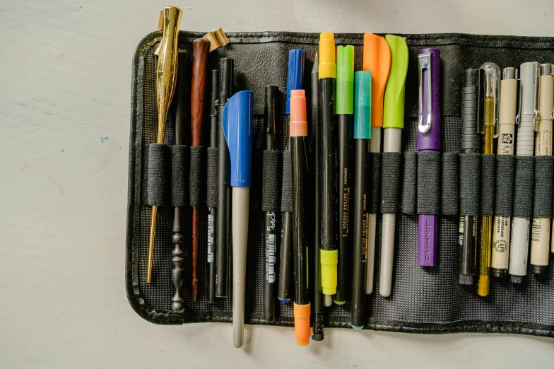 a wallet filled with pens and pencils on top of a table, black marker, thumbnail, handheld, permanent marker