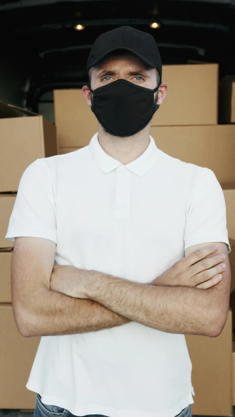 a man wearing a face mask standing in front of boxes, shutterstock, he is wearing a black t-shirt, collar on neck, cover story, leaked image