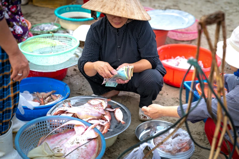 a woman sitting on top of a beach next to buckets of fish, by Julia Pishtar, pexels contest winner, ao dai, filleting technique, two hands reaching for a fish, market stalls