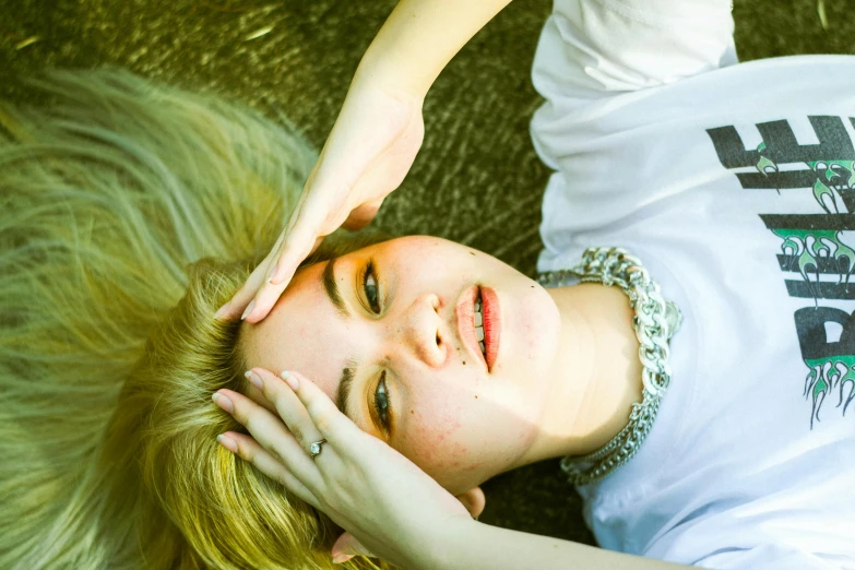 a woman laying on the ground with her hands on her head, inspired by Elsa Bleda, unsplash, magic realism, portrait of kim petras, medium yellow blond hair, ivory pale skin, color photograph portrait 4k