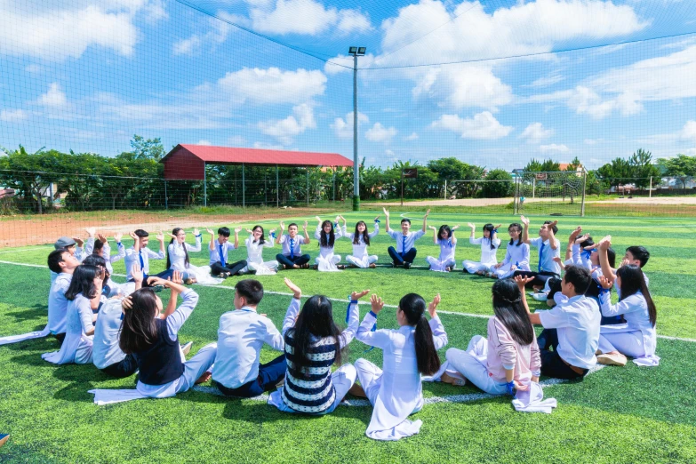 a group of people sitting on top of a soccer field, unsplash, academic art, ao dai, private school, panoramic centered view of girl, yoga