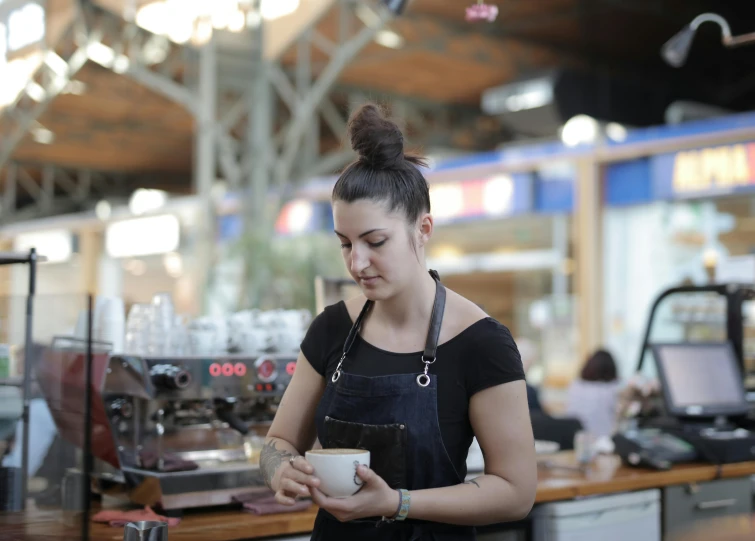 a woman standing in a coffee shop holding a cup, pexels contest winner, greek ameera al taweel, avatar image, maintenance photo, market setting
