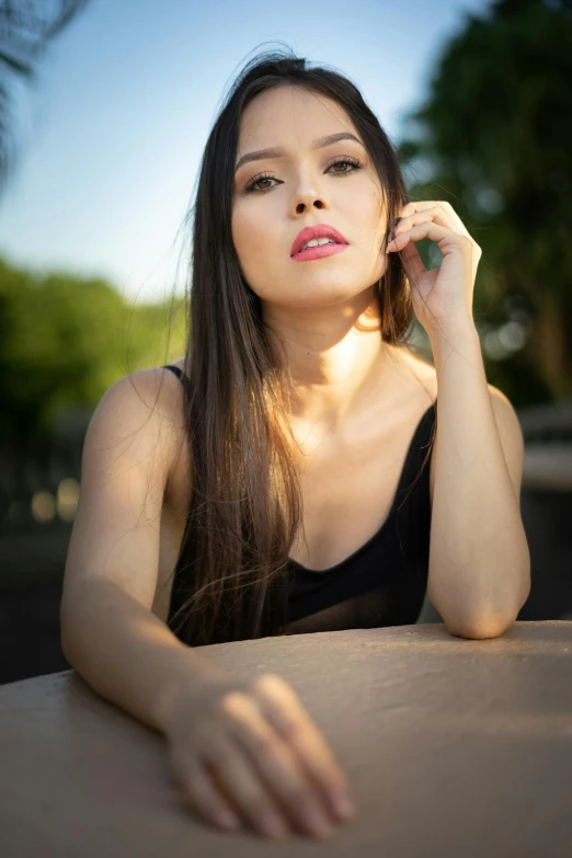 a woman sitting at a table talking on a cell phone, a picture, by Robbie Trevino, beautiful asian woman sitting, she is wearing a black tank top, soft sun lights, dramatic serious pose