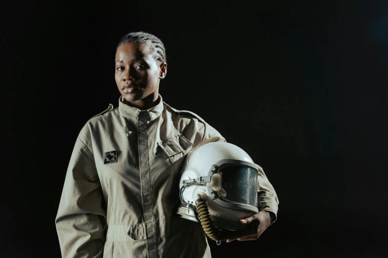 a close up of a person holding a helmet, unsplash, afrofuturism, wearing flight suit, portrait of a female soldier, standing with a black background, piloting a small space shuttle