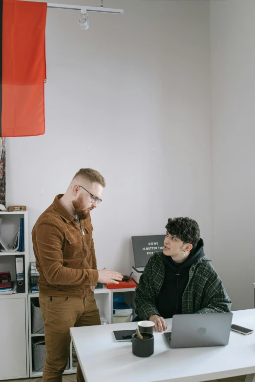 two men sitting at a table working on laptops, by Jacob Toorenvliet, trending on pexels, arbeitsrat für kunst, red flags, standing on a desk, lgbt, looking to his side