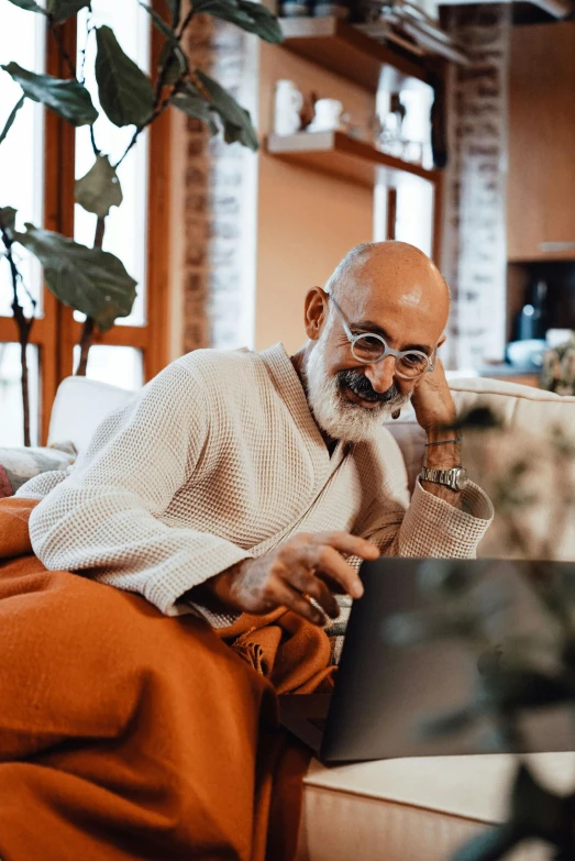 a man sitting on a couch using a laptop, a portrait, inspired by Bapu, trending on pexels, bald with short beard, older woman, gandhi, aboriginal australian hipster