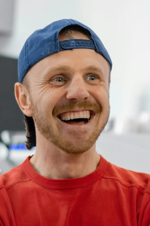 a man in a red shirt and a blue hat, a picture, inspired by Steve Prescott, featured on reddit, he is smiling, portrait kevin mckidd, peter dinklage, 2019 trending photo
