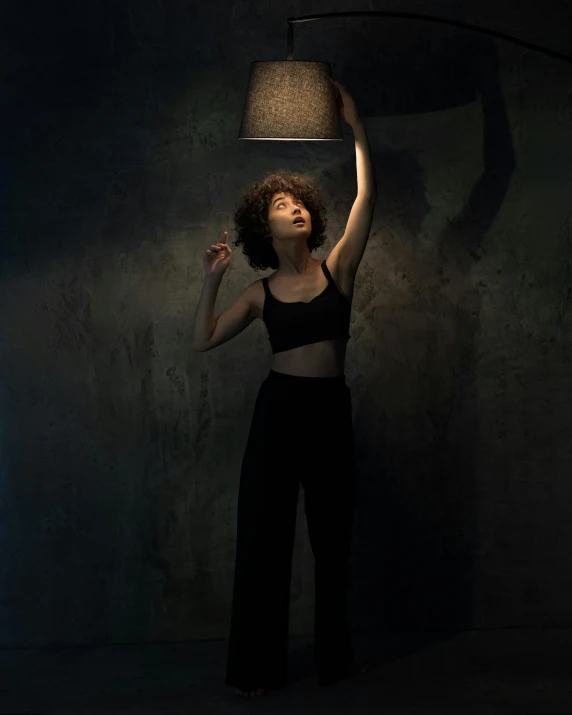 a woman holding a lamp above her head, inspired by Elsa Bleda, magical realism, she is wearing a black tank top, nathalie emmanuel, trending photo, cinematic outfit photo