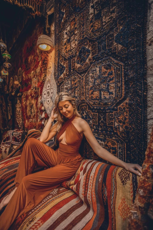 a woman sitting on top of a bed in a room, an album cover, inspired by Riad Beyrouti, trending on pexels, maximalism, orange jumpsuit, persian carpet, 5 0 0 px models, brown