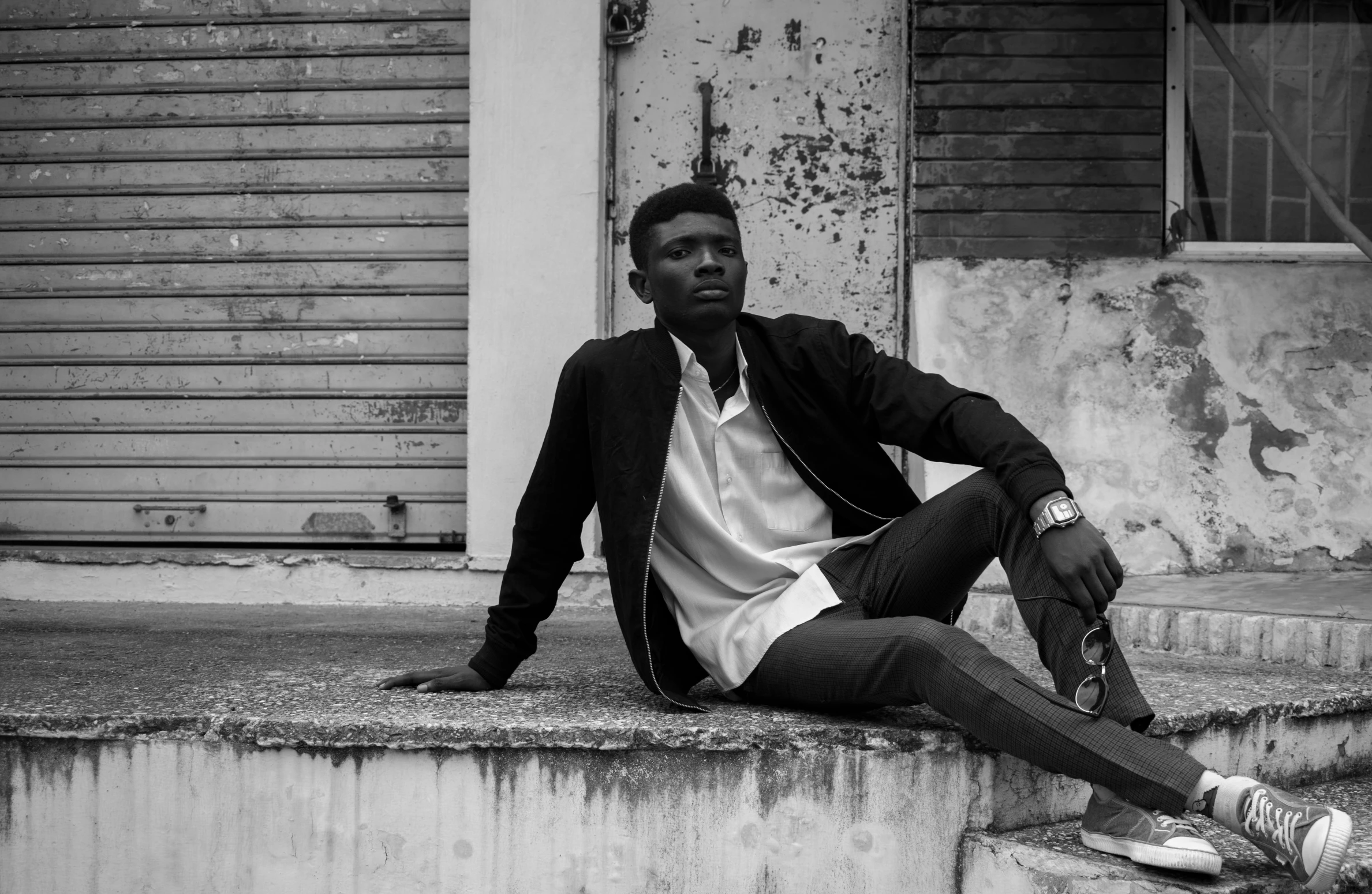 a man sitting on the steps of a building, a black and white photo, by Samuel Silva, pexels, realism, black skin!!!, fashion model pose, wearing a fancy jacket, teenage boy