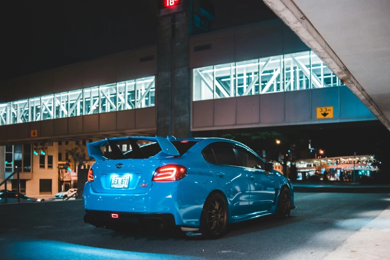 a blue car parked in front of a building at night, rally car, instagram picture, tail lights, set inside of parking garage