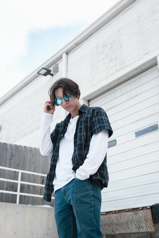 a man standing in front of a building talking on a cell phone, an album cover, unsplash, he wears an eyepatch, flannel, ((blue)), male ulzzang