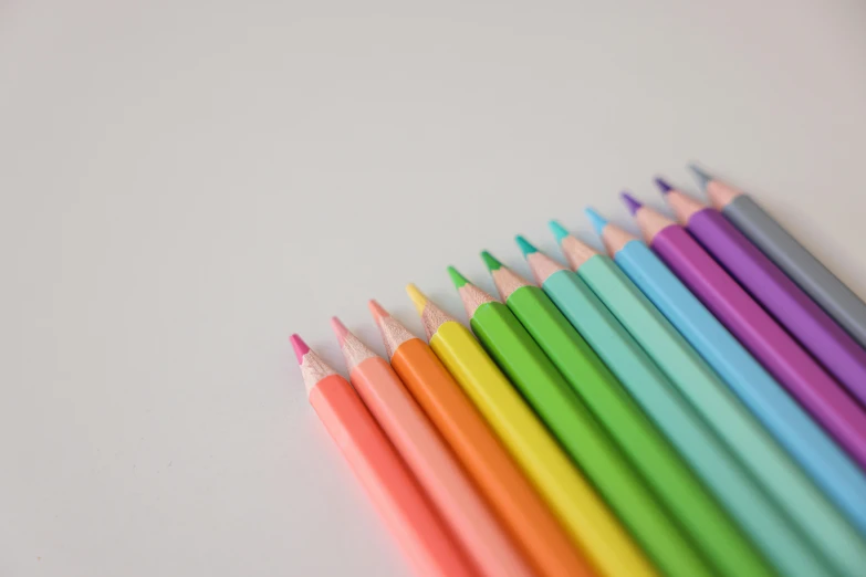 a group of colored pencils sitting on top of a table, a color pencil sketch, by Rachel Reckitt, pexels, neon pastel, set against a white background, low angle photo, colorised