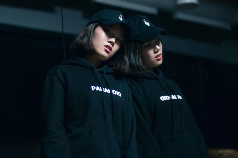 a couple of women standing next to each other, inspired by Wang Duo, trending on unsplash, realism, hat and hoodie, outlive streetwear collection, paranoid, bao pnan