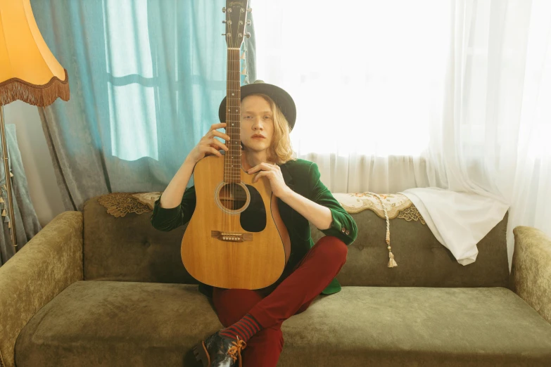 a woman sitting on a couch holding a guitar, sophia lillis, coloured photo, posed, high quality image