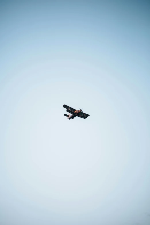 a small airplane flying through a blue sky, a picture, unsplash, suprematism, has black wings, photo taken from the ground, antique, technical