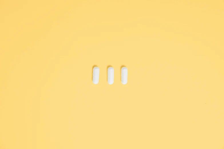 two pills sitting next to each other on a yellow surface, an album cover, inspired by Agnes Martin, trending on pexels, minimalism, the three moiras, white plastic armour, ffffound, uniform teeth