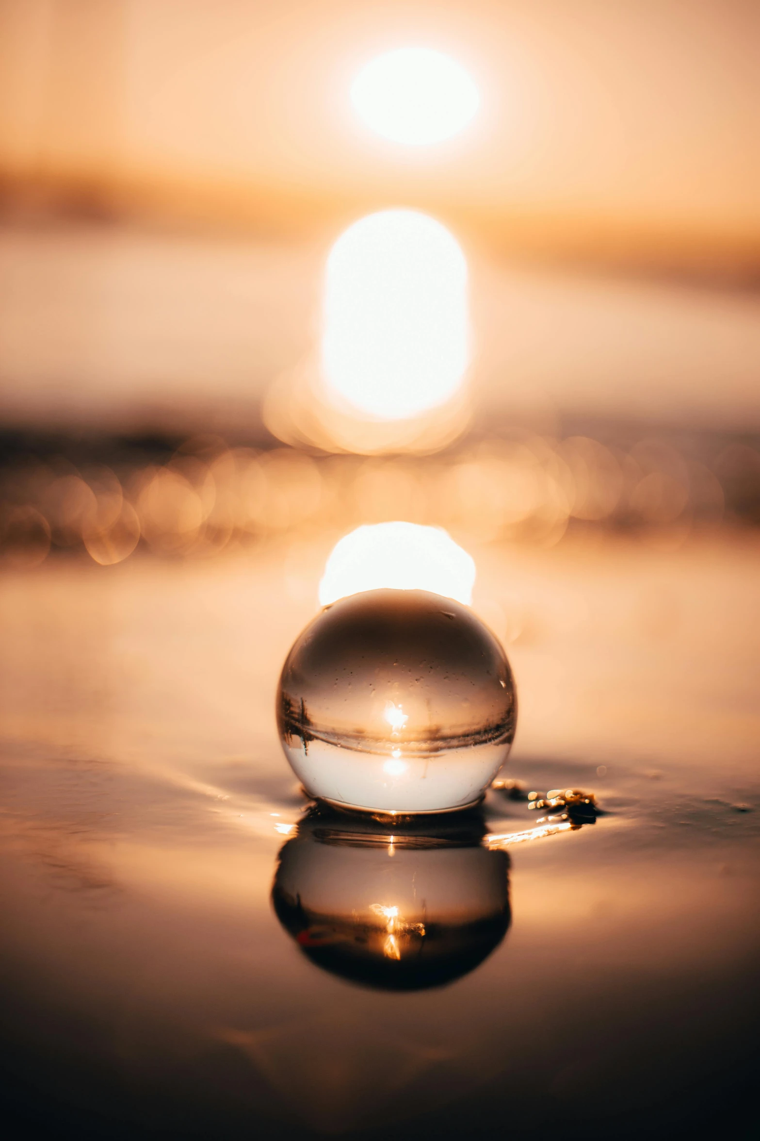 a glass ball sitting on top of a beach, unsplash, light and space, dripping light drops, on a reflective gold plate, dawn light, floating lights