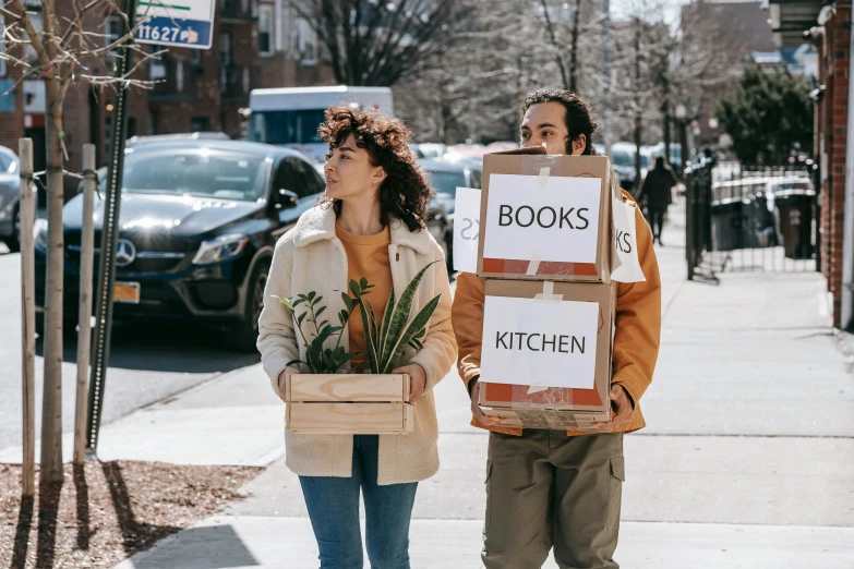 a man and woman walking down a sidewalk carrying boxes of books, a photo, cookbook photo, woman holding sign, urban jungle, avatar image