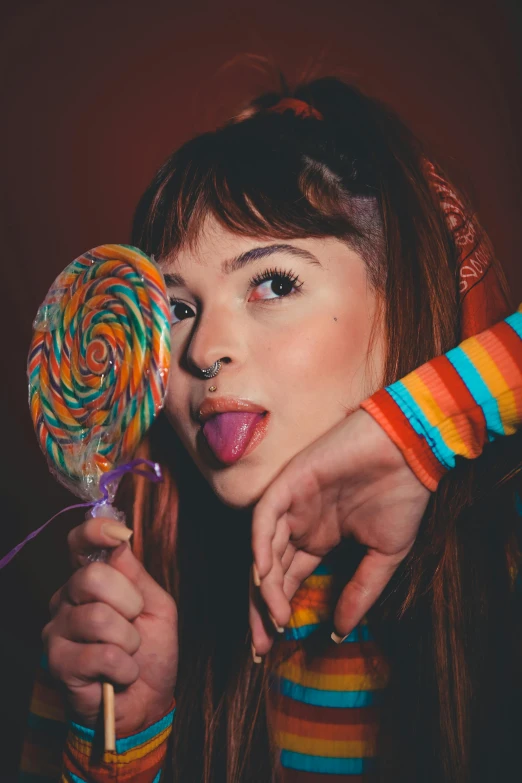 a woman holding a lollipop in front of her face, an album cover, inspired by Glòria Muñoz, brown hair and bangs, colorful]”, rex orange county, headshot profile picture