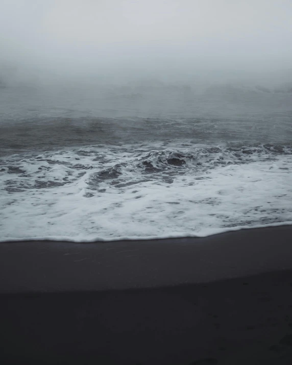 a man standing on top of a beach next to the ocean, a black and white photo, unsplash, romanticism, dark foggy water, an eerie whirlpool, purple sand, a photo of the ocean