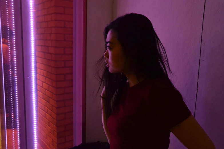 a woman in a red shirt standing in front of a window, inspired by Elsa Bleda, pexels contest winner, realism, purple neon light, young asian girl, looking around a corner, gradients and soft light
