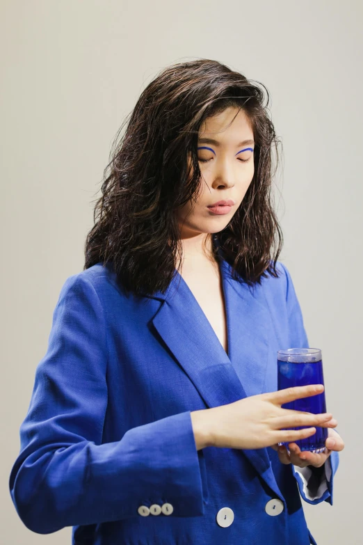 a woman in a blue suit holding a glass of water, an album cover, inspired by Yves Klein, trending on pexels, asian female water elemental, concerned expression, ultraviolet, hito steyerl