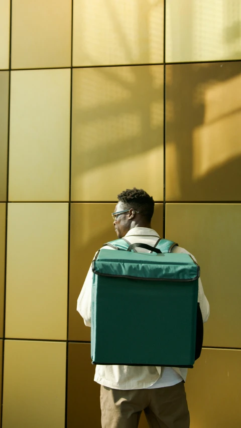 a man with a suitcase standing in front of a building, by Andries Stock, pexels, green and gold, square backpack, sitting in a waiting room, jaylen brown