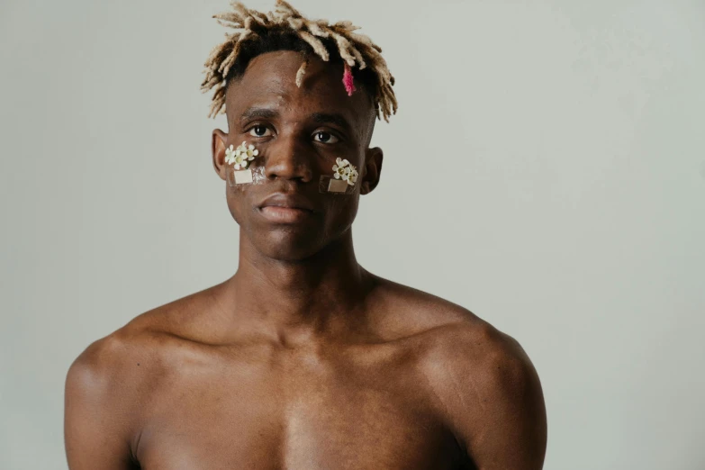 a man with dreadlocks standing in front of a white wall, inspired by Terrell James, trending on pexels, afrofuturism, flowers on heir cheeks, wearing loincloth, messy blond hair, covered in bandages