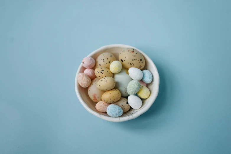 a bowl filled with mini eggs on top of a blue surface, unsplash, with celadon glaze, various posed, snacks, set against a white background