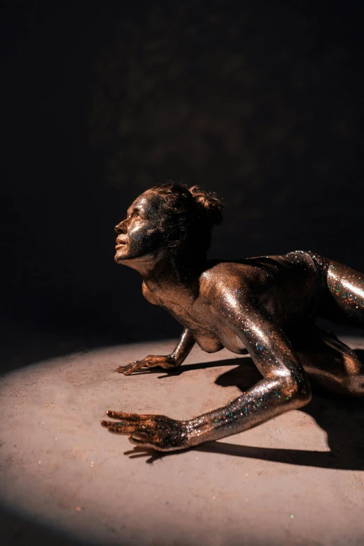 a bronze statue of a woman laying on the ground, a bronze sculpture, trending on unsplash, figurative art, glowing with silver light, lizard pose, body painted with black fluid, made of wax and oil